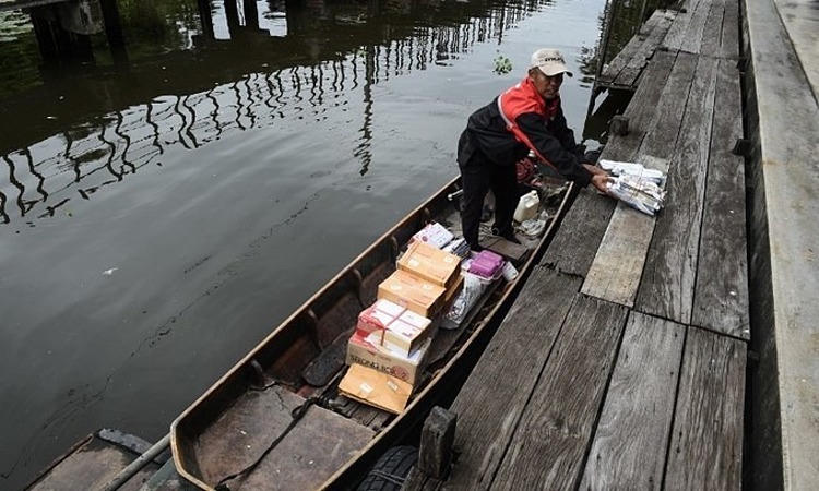 Một bưu tá vận chuyển thư và bưu kiện bằng thuyền trên con kênh ở quận Bang Khun Thian, ngoại ô Bangkok, hôm 17/7/2017. Ảnh: AFP